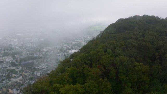 Aerial views reveal fog enveloping Salzburg's skyline, with Monchsberg lush greenery in the foreground. A tranquil ambiance surrounds the city's historic architecture