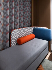Stylish hotel sofa featuring a geometric patterned backrest, gray upholstery and a vibrant orange...