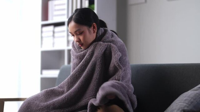 Young woman shivering under blanket on couch