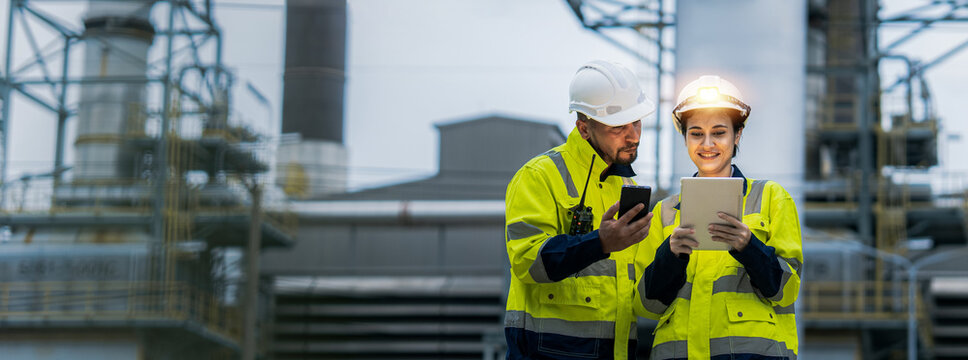 Male and female industrial engineers wearing hard hats talk to collaborate on new project. Team of engineers inspecting gas separation plant using tablets.