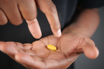 A person is holding a yellow pill delicately with their fingers while pointing at it,
