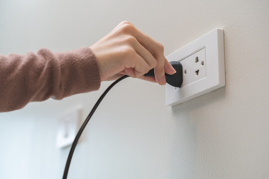 Hand of woman plugged in, unplugged electricity cord cable at home, put on or remove electric plug cable in socket on wall outlet for saving, control power electrical energy, eco environment concept.