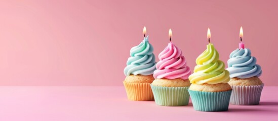 Colorful cupcakes with lit candles are beautifully arranged on a pink background, ideal for birthdays and celebrations. These festive and delicious treats are enticing and sure to please