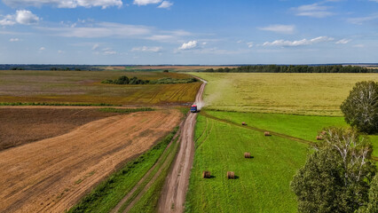 The truck is driving along a dusty country road through green fields with rolls of hay