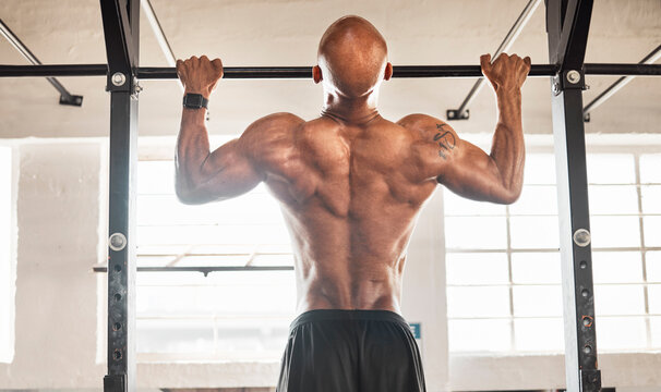 Man, back or fitness with pull ups at gym for strength, muscle gain or workout on equipment. Active, muscular or strong male person hanging or lifting body weight for training exercise at health club