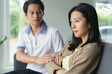 Asian couple having relation problem. Wife crying and sitting separate with her husband at home after quarrel.