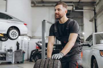 Happy Car Mechanic holding a tire at the repair garage. Replacement of winter and summer tires