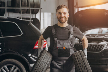 Preparing for a season. Happy Car Mechanic holding a tire at the repair garage. Replacement of winter and summer tires