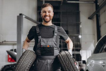 Happy Car Mechanic holding a tire at the repair garage. Replacement of winter and summer tires © anatoliycherkas