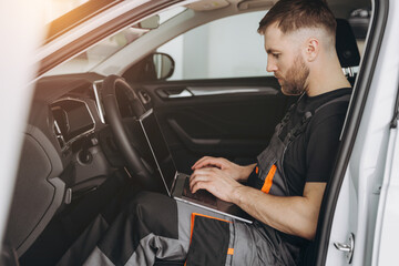 Automotive mechanic running diagnostics software on computer. Mechanic sitting in car and working...