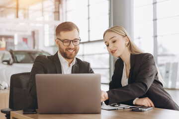 Sitting by the table and taking the keys. Man with woman in white clothes are in the car dealership together. Car sales contract