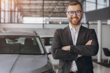 Portrait of Modern car seller standing in car salon with arms crossed with copy space