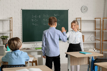 Cute children giving high-five to each other in classroom