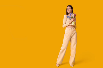 Happy smiling young woman with hyacinth flowers on yellow background