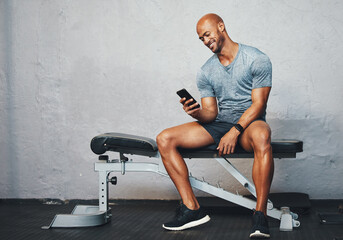 Fitness, gym and bench with African man on phone with exercise tracker and smile at wellness club. Happy, mockup and break with health insurance login to post training results for online reward