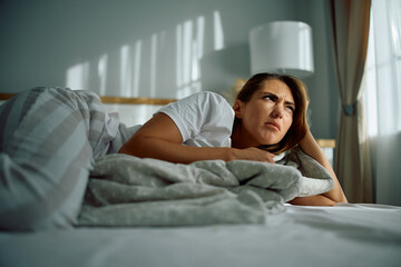 Displeased woman lying down on bed at home.