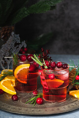 Cranberry boozy Christmas cocktail with ice and rosemary on dark background. Festive spiced drink with orange, berry, cinnamon and anise.
