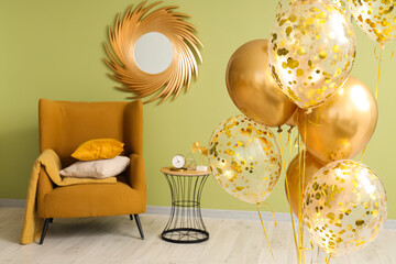 Golden air balloons, armchair and table near green wall in room