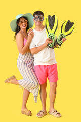 Happy young couple with flippers and snorkeling mask on yellow background