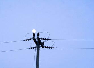 The blue sky at dusk with the moon shining on the top of the electric pole like a light bulb.