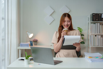 Confident Asian businesswoman working and checking work with laptop, holding files and smiling. Happy and successful Technology and relaxing coffee drinking at modern office.