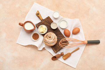 Wooden board with sweet cinnamon roll and different ingredients on beige background