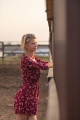 Portrait of a beautiful blonde girl in a red dress on a ranch.