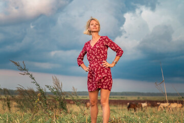 Portrait of a beautiful blonde girl in a red dress on a ranch.