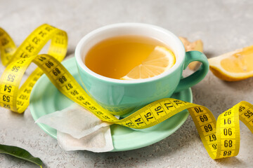 Cup of diet tea with lemon slice and measuring tape on grunge background. Weight loss concept