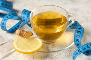 Cup of tea for weight loss and measuring tape on white grunge table, closeup