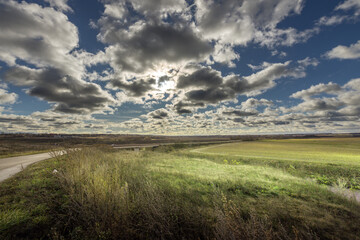 A field with a road in the foreground and a cloudy sky in the background