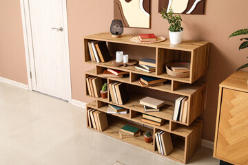 Modern shelving unit with books, houseplants and home decor near brown wall