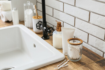 Bath accessories and modern sink on table near white brick wall in bathroom