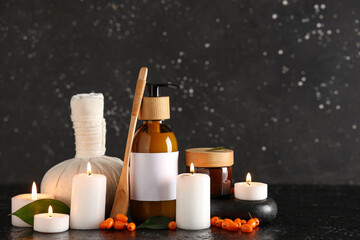 Composition with natural cosmetic products, herbal massage bag, burning candles and sea buckthorn on dark background