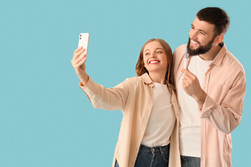 Happy young couple with pregnancy test taking selfie on blue background