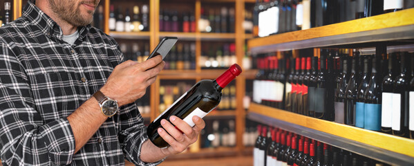 Male customer in wine shop holding wine bottle and scanning e-label using smartphone.