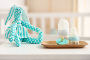 Bottles with baby milk formula, pacifier and toy bunny on light table in children's room