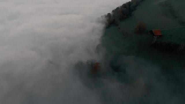 Drone flight over a hilly landscape with an abandoned barn. It's autumn and foggy. There is a mystical atmosphere.