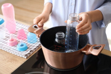 Woman sterilizing baby bottles in kitchen