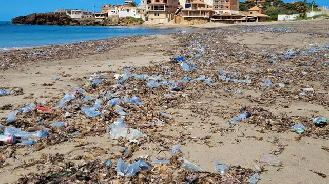 Revealing shot of plastic trash and pollution on a Mediterranean beach with village houses in the background and an ocean view in the Azeffoun region of Algeria
