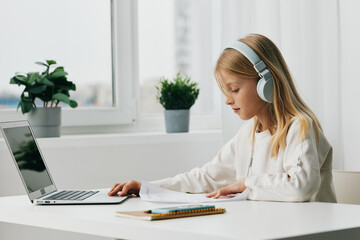 Young girl smiling while using a laptop for elearning at home She is sitting at a table, surrounded by schoolbooks and a notebook The girl is fully engaged in her online studies, typing on the