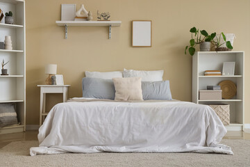 Stylish interior on bedroom with comfortable bed, bedside table and shelving units