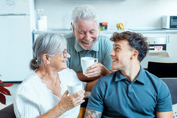 A young man spends time with his elderly grandparents in a pleasant home setting, enjoying laughter and togetherness while creating warm family memories in a comfortable and supportive environment