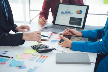Business Professionals Analyzing Data: A close-up shot of a diverse team of business professionals gathered around a table, analyzing data and charts on a laptop and tablet. The scene conveys focus.