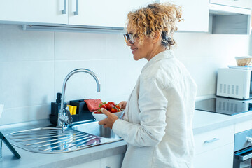 Mature woman in her home kitchen preparing a healthy snack with fresh strawberries and fruit, showcasing a cheerful approach to daily domestic duties while maintaining a wellness-focused lifestyle