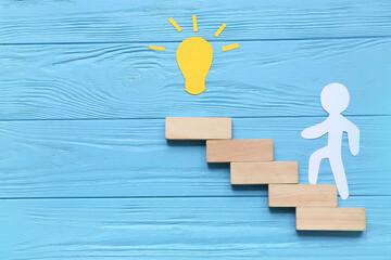 Paper human figure with light bulb and blocks on blue wooden background. Coaching concept