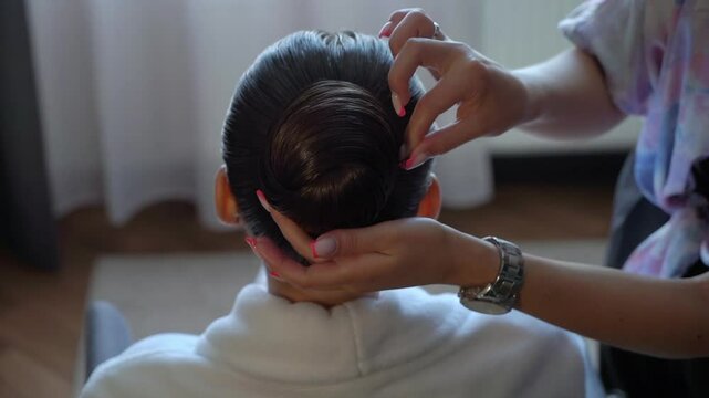 A closeup view of a skilled hairstylist meticulously working on a chic bun hairstyle for an elegant look and finish