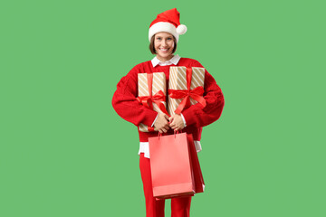 Beautiful young happy woman in Santa hat with shopping bags and gift boxes on green background. Christmas celebration