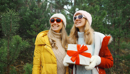 Happy smiling women friends, gift box, celebration on Christmas tree background in winter forest