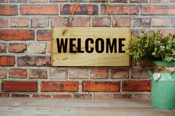 Welcome Home text on wooden sign hanging on old brick wall background